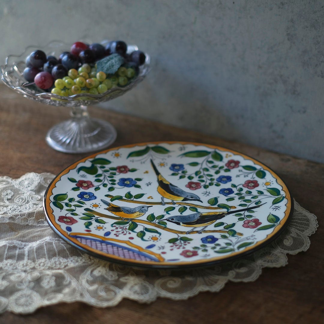 スペイン アンティーク手描き飾り皿 鳥と花の多色絵付け レースクロスとガラスコンポートを背景にした正面スタイリング写真